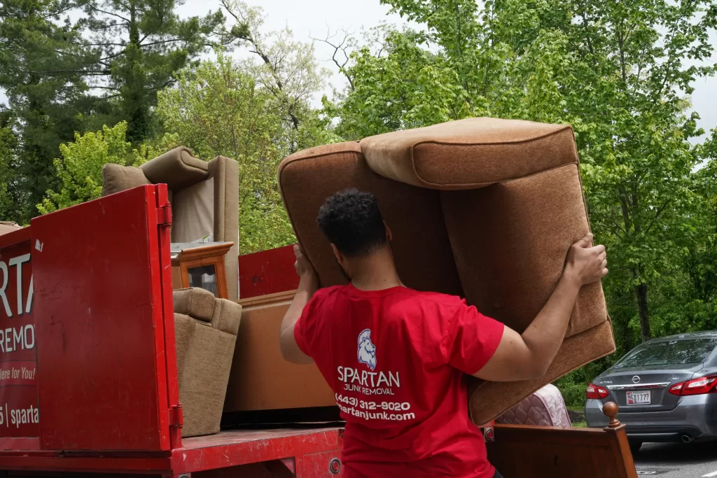 A Spartan Junk Removal Team Member Putting Furniture In The Back Of Our Truck.